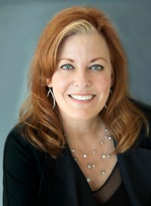 A formal headshot of Britt Lopez, featuring a woman with red hair and a black blazer, suitable for business purposes.